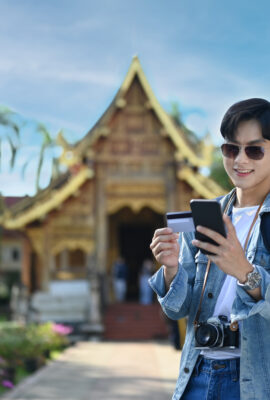 Smiling man tourist holding credit card and using smartphone for payment online or checking his bank account.